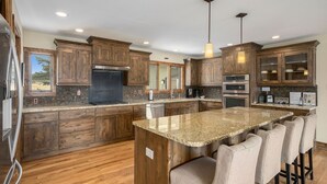 Una cocina moderna con armarios de madera, encimeras de granito, una isla central con taburetes de bar y electrodomésticos integrados.