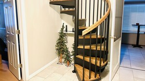 Una escalera espiral moderna con escalones de madera y barandillas de metal, que conduce a un piso superior.