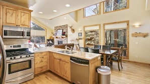 Una cocina amplia con armarios de madera, electrodomésticos de acero inoxidable, una isla grande con un fregadero y un comedor con mesa y sillas.
