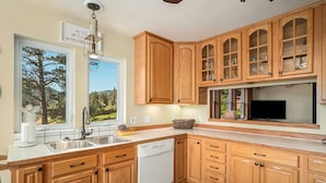 Una cocina con armarios de madera, lavavajillas, pileta y ventana con vista a árboles.