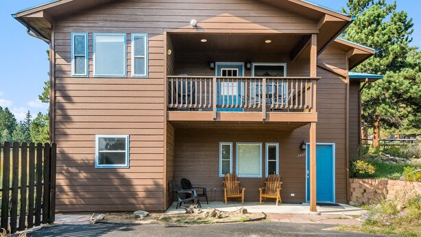 A two-story building with a balcony, a blue door, and two chairs outside.
