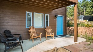 A wooden house with a porch, two wooden chairs, and a black chair.