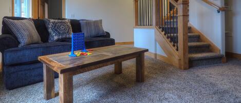 Un salón con un sofá azul oscuro, una mesa de centro de madera y una escalera con barandillas de madera.