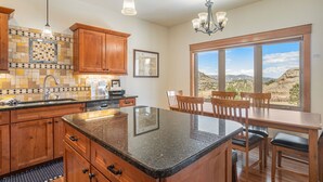 Una cocina con armarios de madera, encimera de granito y comedor con vistas a las montañas.