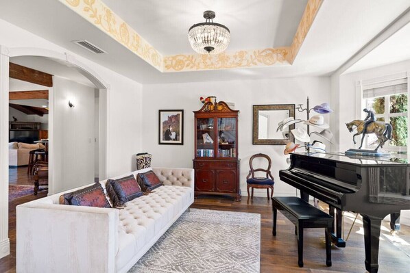 A living room with a white sofa, a black piano, a wooden cabinet, and a chandelier.