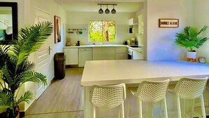 A modern kitchen with a central island, white bar stools, and a view of the outdoors through a window. - Villa Magellan — Charme, Espace & Plage à 250 m (Baie Orientale) (Orient Bay)
