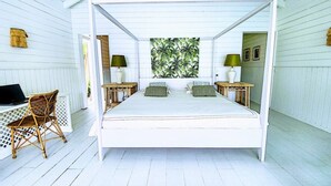 A white four-poster bed with a view of a tropical garden, a wooden desk with a chair, and two nightstands with lamps. - Villa Horizon Lointain . Plage & piscine privée (Cul-de-Sac)