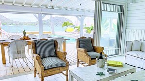 A sunlit room with wicker chairs, a white sofa, and a pool view. - Villa Horizon Lointain . Plage & piscine privée (Cul-de-Sac)