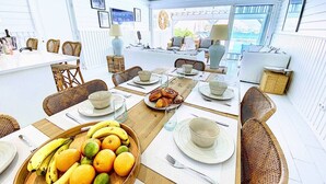 A spacious dining area with a long table set for breakfast, featuring wicker chairs, a fruit bowl, and a view of the outdoors. - Villa Horizon Lointain . Plage & piscine privée (Cul-de-Sac)