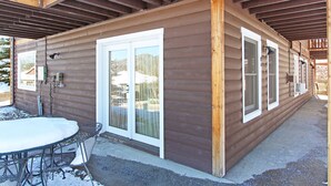 Une cabane en bois dotée d’un patio couvert, d’une porte-fenêtre coulissante et d’une table en métal avec des chaises.
