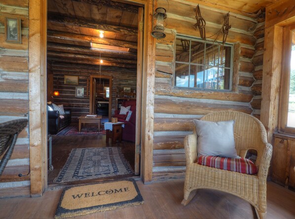 Interior de una cabaña de madera con una silla de mimbre, un sofá rojo y una mesa de centro de madera.