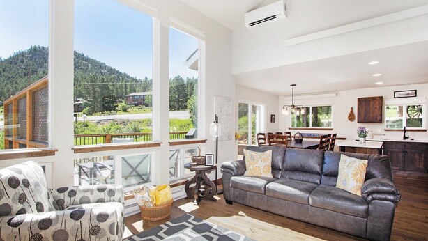 A spacious living room with a large gray sofa, patterned armchairs, and a dining area with a wooden table and chairs.