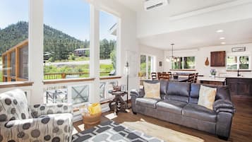 A spacious living room with a large gray sofa, patterned armchairs, and a dining area with a wooden table and chairs.