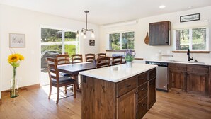 A modern kitchen with wooden cabinets, a central island, and a dining area with chairs.
