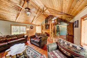 Ein geräumiges Wohnzimmer mit Holzbalkendecke und Deckenventilator, mit gemusterten Sofas und einem Couchtisch.