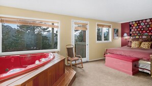 A bedroom with a large window, a red bathtub, a wooden rocking chair, and a bed with a floral-patterned headboard. - Deering Crest – 3BR Home with Panoramic RMNP Views – Windcliff – 20-NCD3249 (Estes Park)