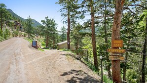 A dirt road leading to a cabin with a sign indicating directions to nearby locations. - Deering Crest – 3BR Home with Panoramic RMNP Views – Windcliff – 20-NCD3249 (Estes Park)