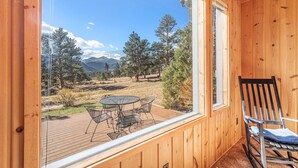 A wooden cabin with a deck, a table with chairs, and a rocking chair.