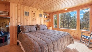 A wooden cabin bedroom with a large bed, bookshelves, and a rocking chair.