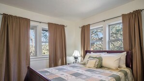 Ein Schlafzimmer mit einem Holzbett, einem Nachttisch mit Lampe und fensterbepfungen.