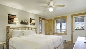 Une chambre avec un grand lit, un ventilateur de plafond, une porte en bois et une fenêtre donnant sur un beau paysage.