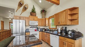A kitchen with wooden cabinets, granite countertops, a refrigerator, microwave, and a coffee maker.