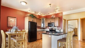 A modern kitchen with wooden cabinets, a black refrigerator, a microwave, and a dining area with wooden chairs.