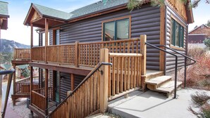 A log cabin with a wooden deck, a staircase, and a window.
