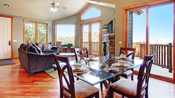 A spacious living area with a glass-top dining table, comfortable seating, and large windows offering a view of the outdoors.