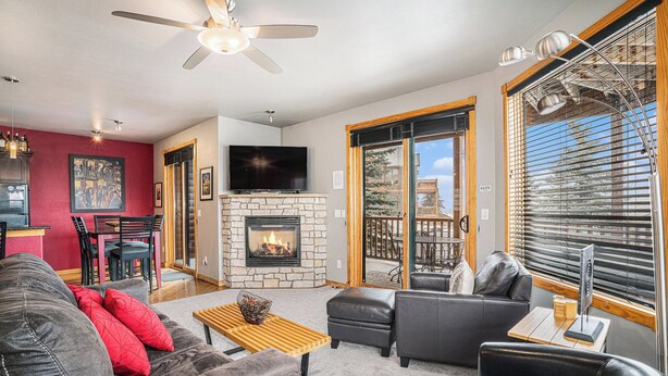 A modern living room with a stone fireplace, leather sofas, a wooden coffee table, and a large TV.
