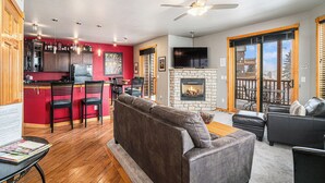 A modern living room with a fireplace, a dining area with red walls, and a kitchen with wooden cabinets and a bar.