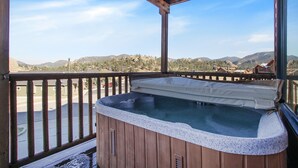 A hot tub on a wooden deck with a view of mountains and houses.