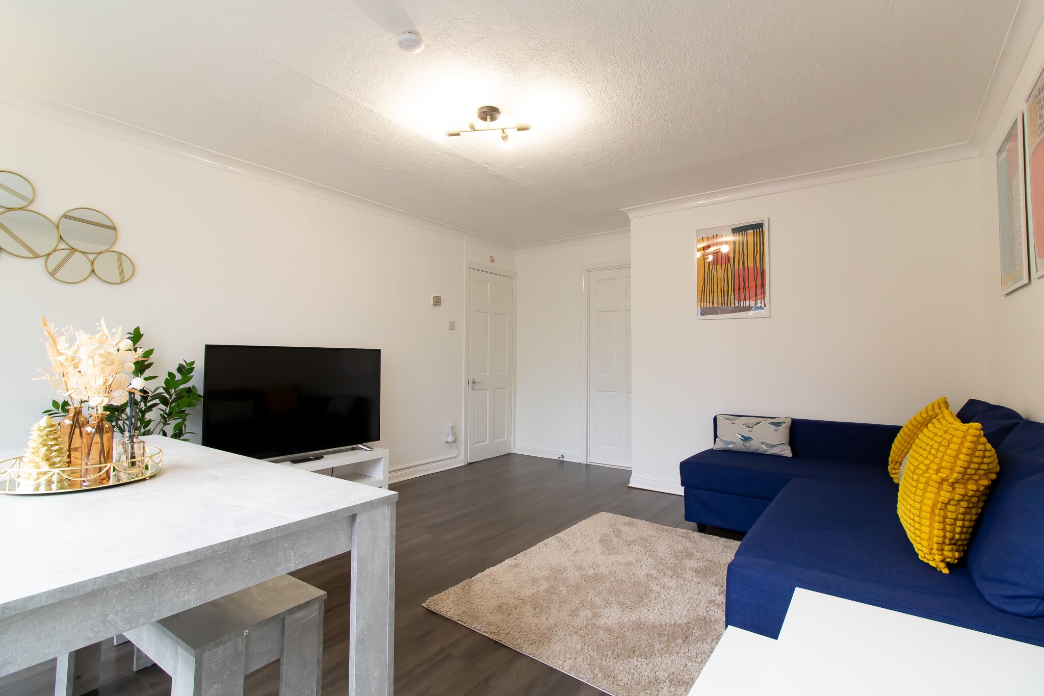 A modern living room with a flat-screen TV, a blue sofa, and a white coffee table.