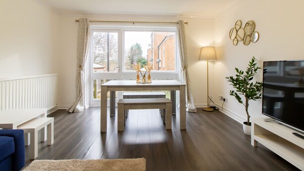A modern living room with a dining table, bench, sofa, TV, lamp, and potted plant. - Stunning 2-bed Apartment in Washington (Washington)