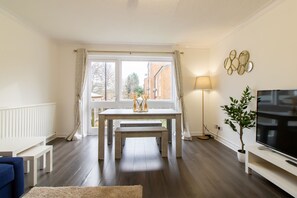 Ein modernes Wohnzimmer mit Esstisch, Bank, Sofa, Fernseher, Lampe und Zimmerpflanze.