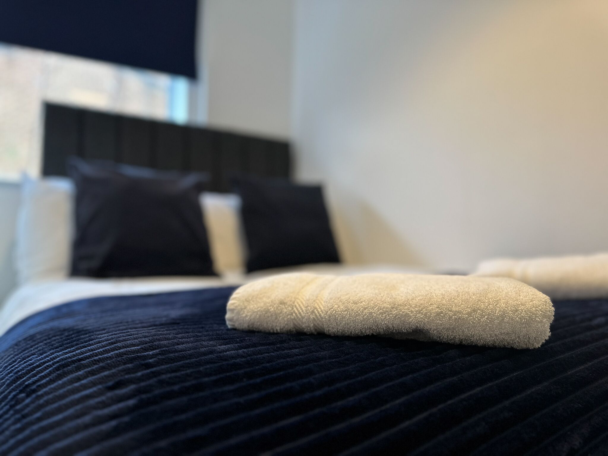 Una cama con un edredón azul oscuro y dos toallas blancas.