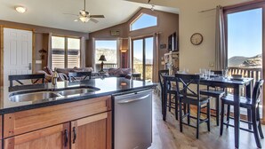 A kitchen with a dishwasher, a dining area with chairs and a table, and a large window with a view of the mountains.