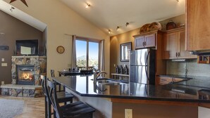 A modern kitchen with a stone fireplace, stainless steel appliances, and a large island.