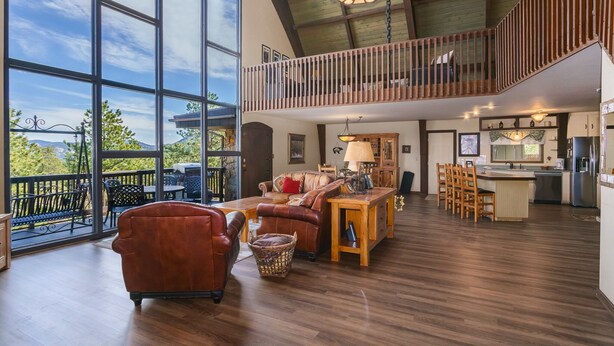 A spacious living area with a large window, a wooden dining table, and a kitchen area.