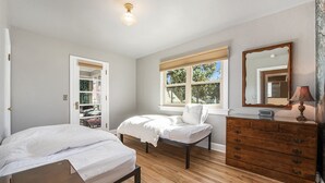 Ein Schlafzimmer mit Bett, Kommode, Spiegel und einem Fenster mit Jalousien.