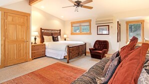 A bedroom with a wooden bed, a nightstand, a red armchair, a sofa, a ceiling fan, and a window.