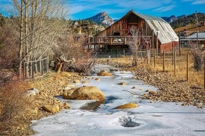 A wooden cabin with a metal roof, a wooden deck, and a river running through a rocky landscape.