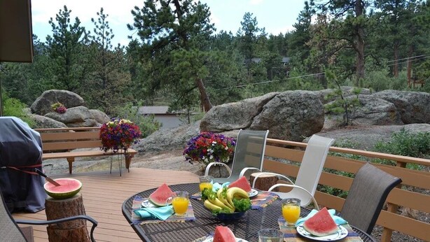 Un espace de restauration en plein air avec une table ronde dressée pour deux personnes, agrémentée de tranches de pastèque, d’un saladier de fruits et de verres de jus d’orange.