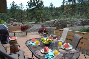 Un espace de restauration en plein air avec une table ronde dressée pour deux personnes, agrémentée de tranches de pastèque, d’un saladier de fruits et de verres de jus d’orange.