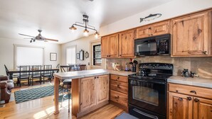 Une cuisine avec des meubles de rangement en bois, un poêle noir et un ventilateur de plafond.