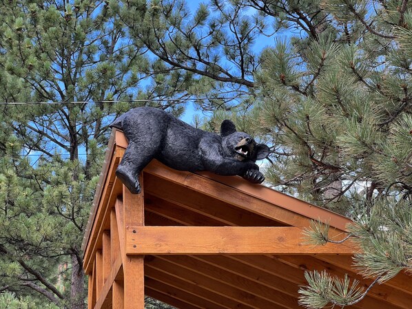 A bear statue on a wooden structure with a clear view of pine trees in the background.