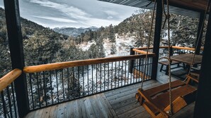 A wooden deck with a view of snow-covered mountains and a forest.