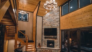 A spacious living room with a stone fireplace, wooden ceiling, and a large black leather sofa.