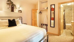 A hotel room with a bed, a wooden door, a bathroom with a shower, and a mirror.
