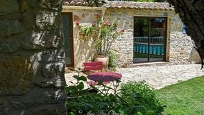 Un bâtiment en pierre doté d’une terrasse, d’un banc rouge et d’un pot de fleurs.